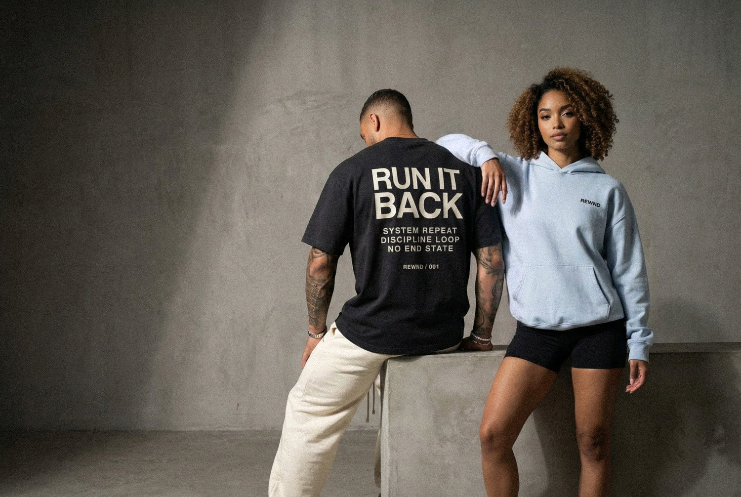 Two people wearing rewnd clothing against a gray background